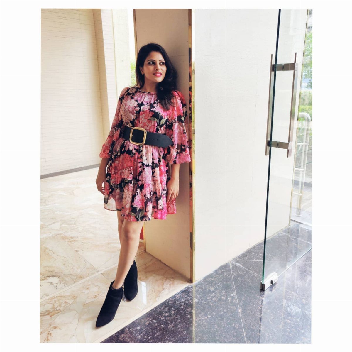 Woman in a pink floral dress and black ankle boots posing in a hallway.