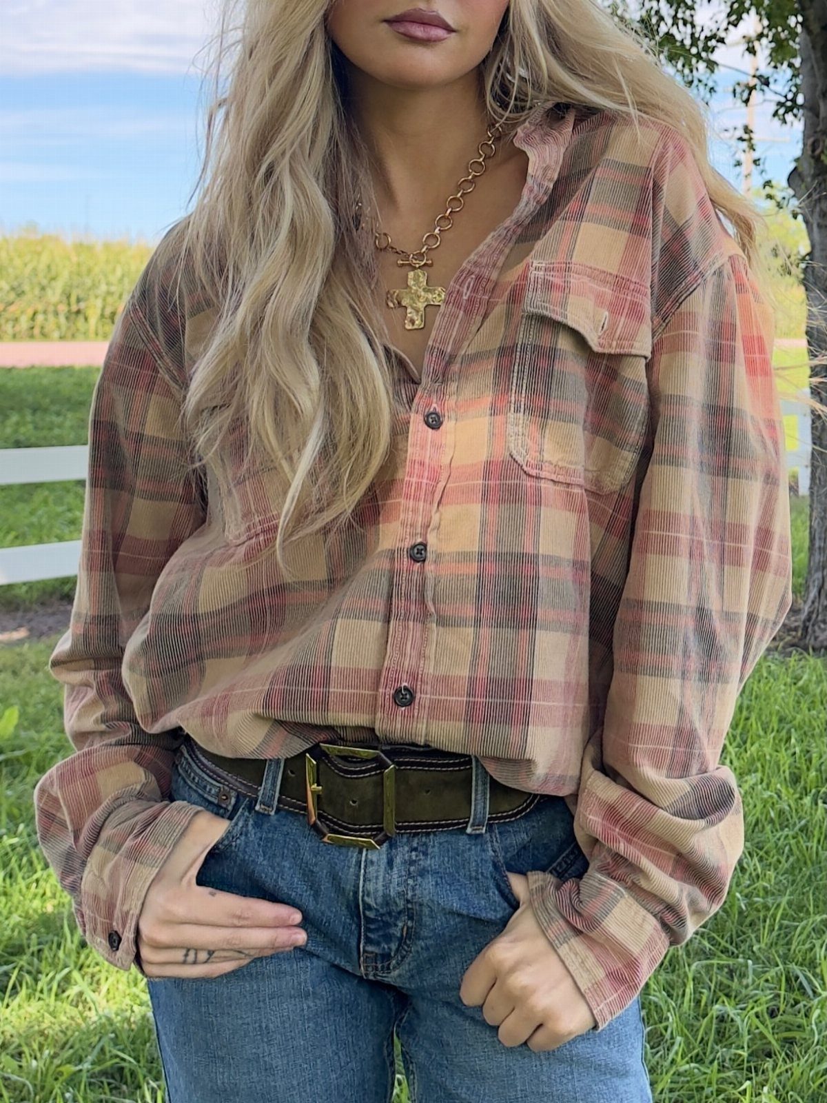 Woman wearing a tan plaid shirt and blue jeans in a grassy field.