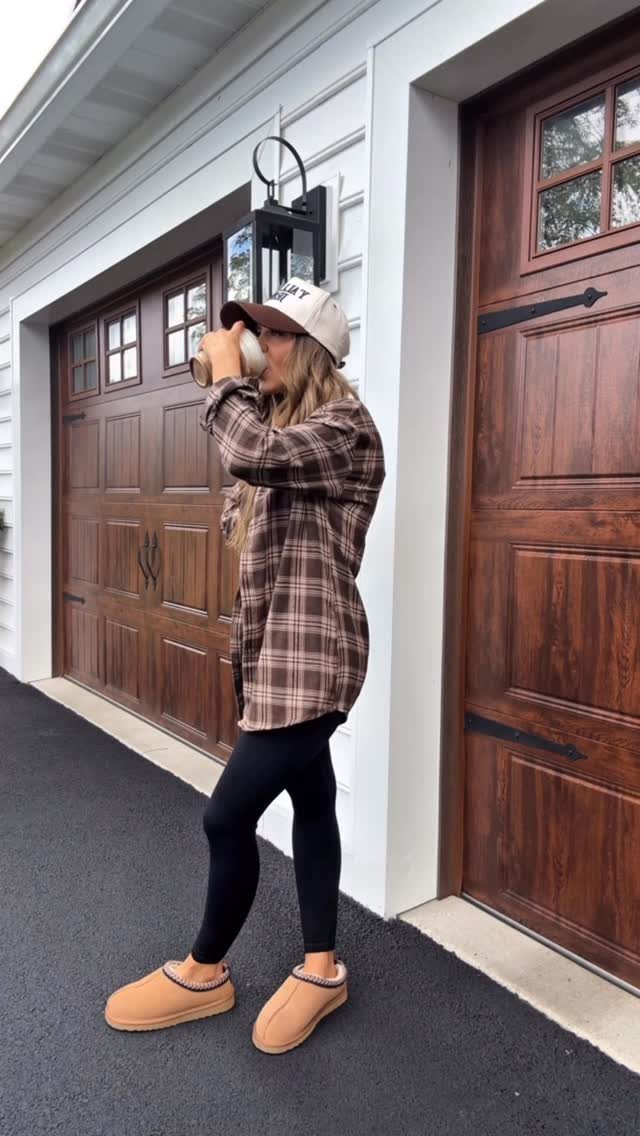 Woman in plaid shirt, black leggings, and tan shoes standing by garage doors.