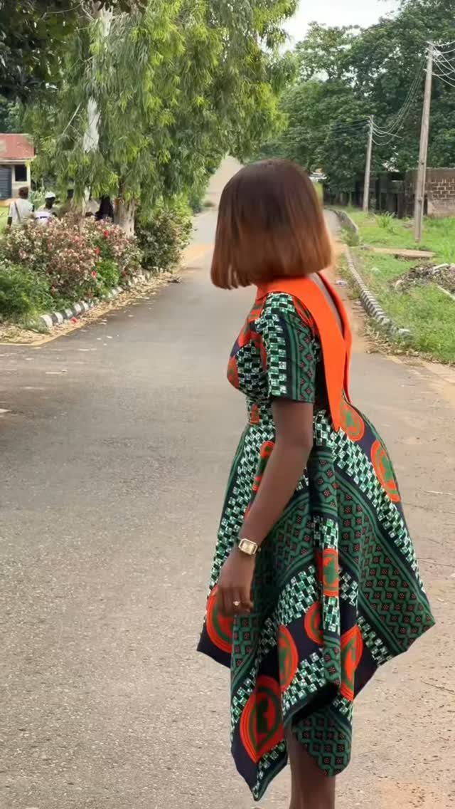 Woman wearing a green and orange patterned Ankara dress with a fitted waist.