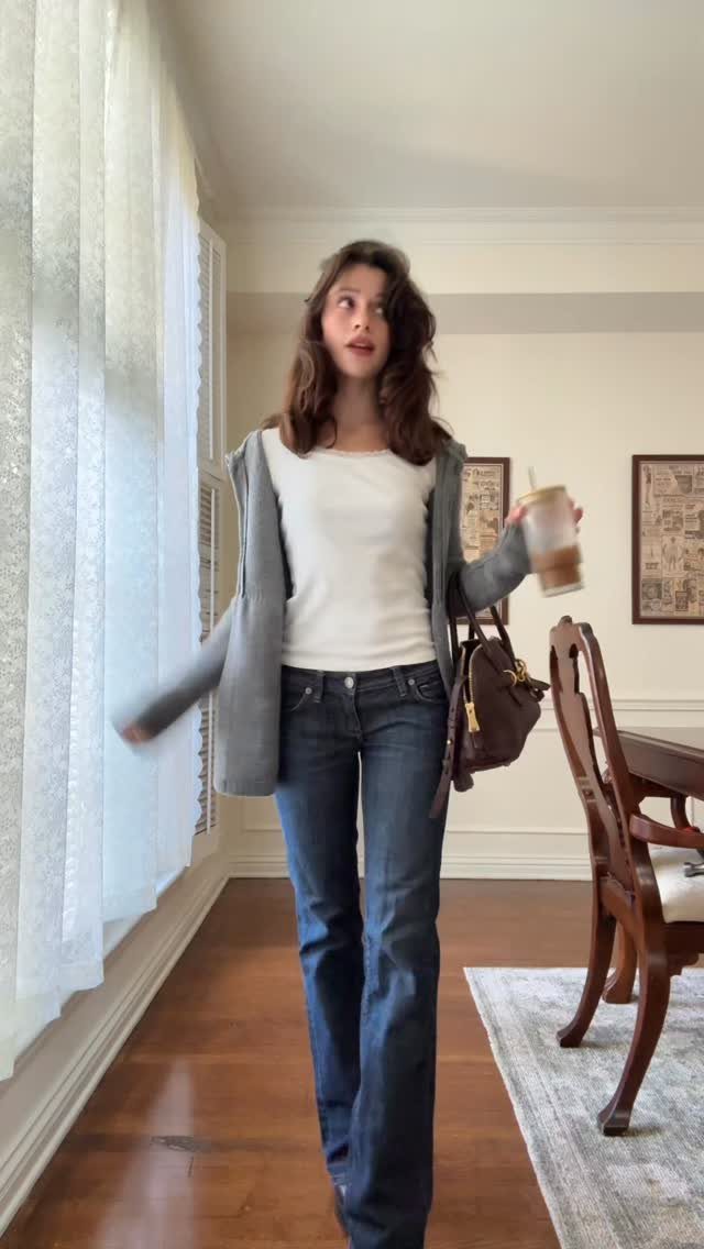 Woman wearing a grey cardigan, white tee, and dark blue straight-leg jeans indoors.