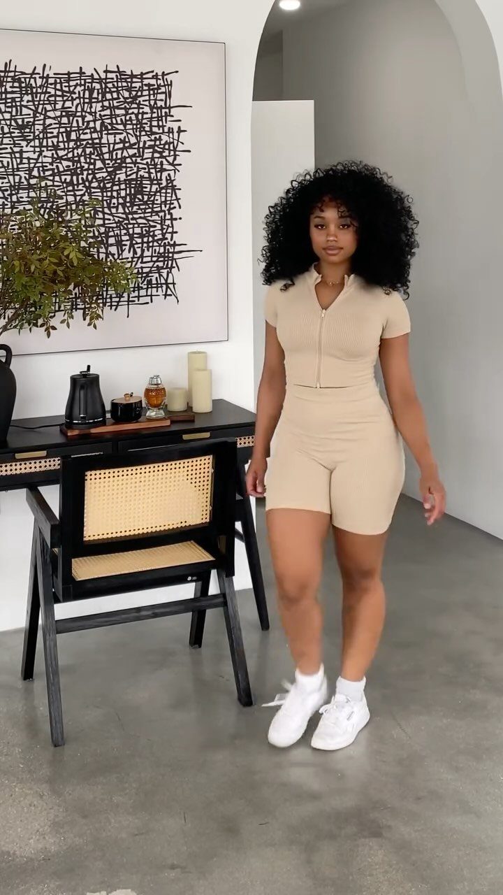 Woman with curly hair wearing a beige matching set and white sneakers indoors.