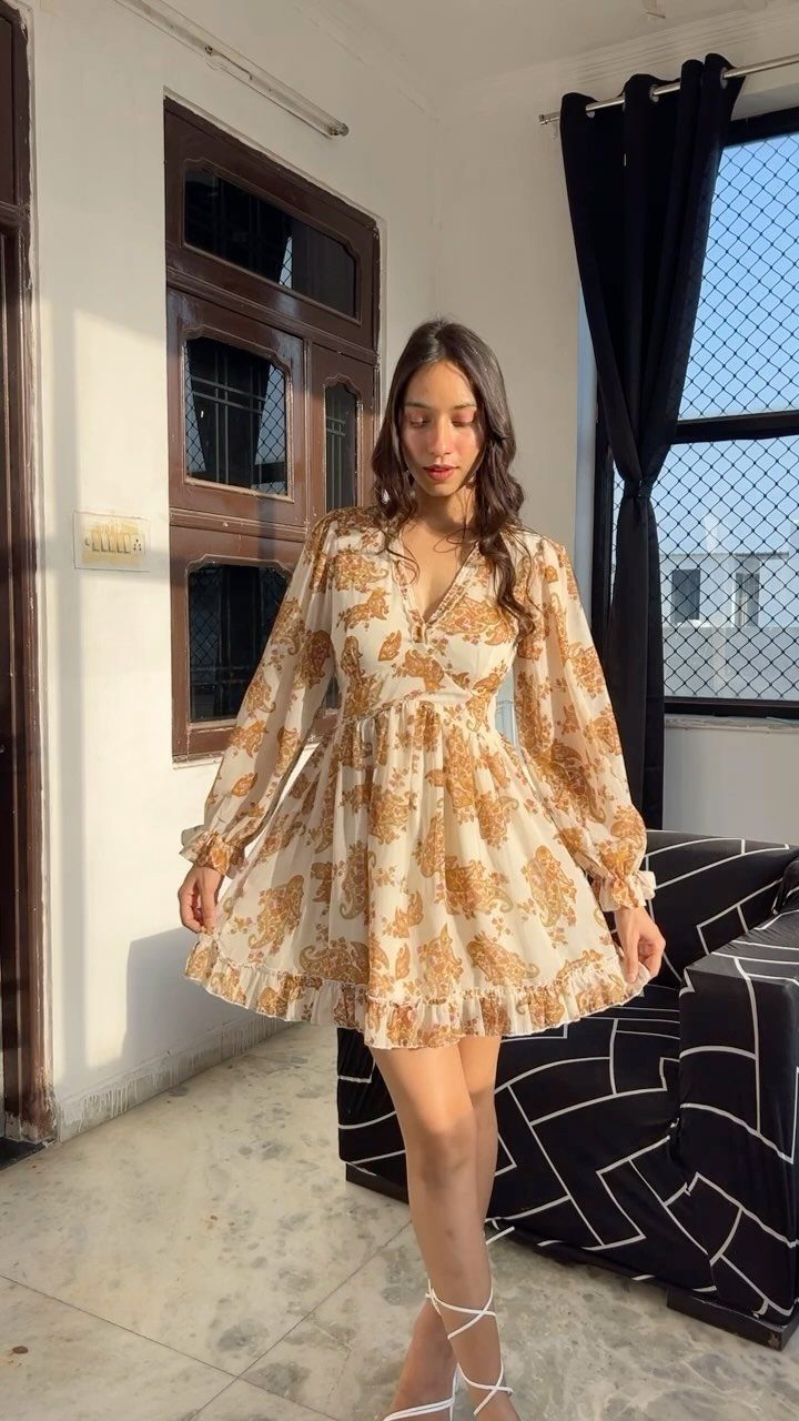 Woman wearing a short gold floral fit-and-flare dress with long sleeves.