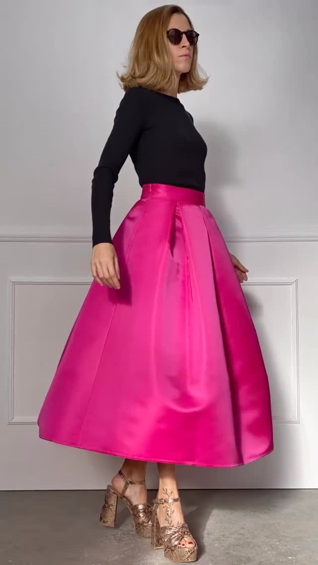 Woman wearing a bright pink high-waisted satin skirt and black long-sleeved top.