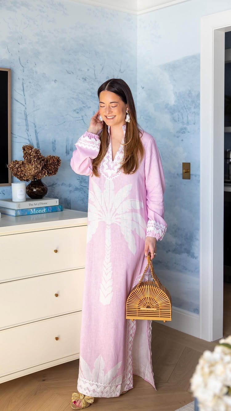 Woman wearing a pink palm tree print maxi dress and holding a bamboo bag.