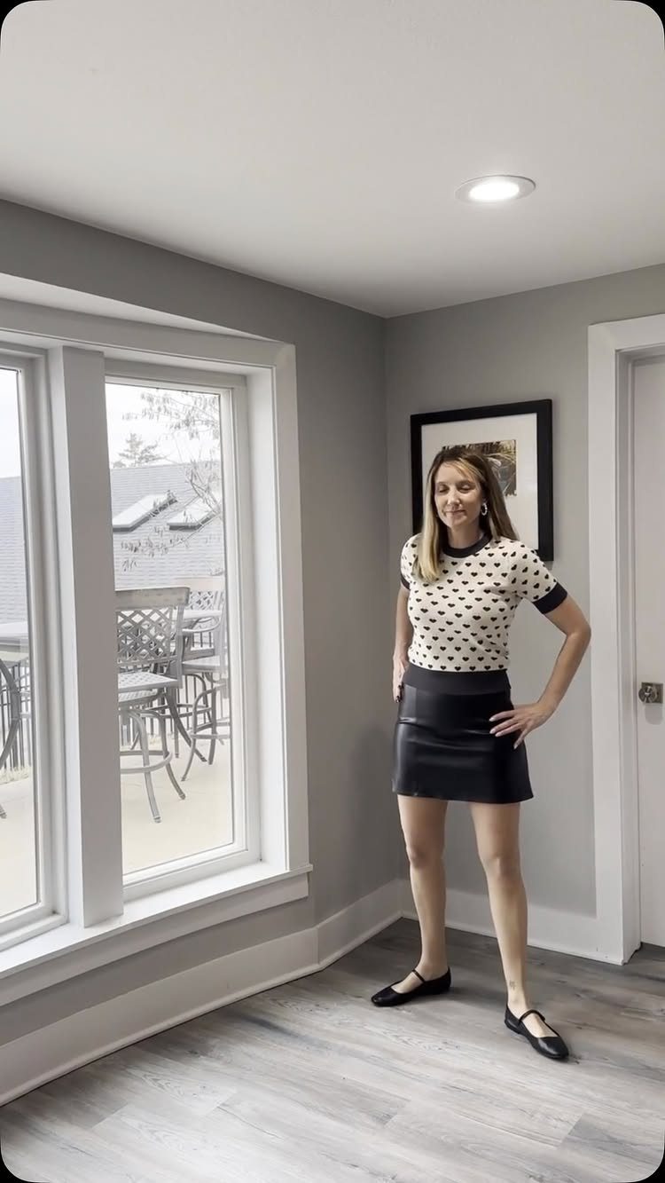Woman wearing a polka dot top and black leather mini skirt in a room.