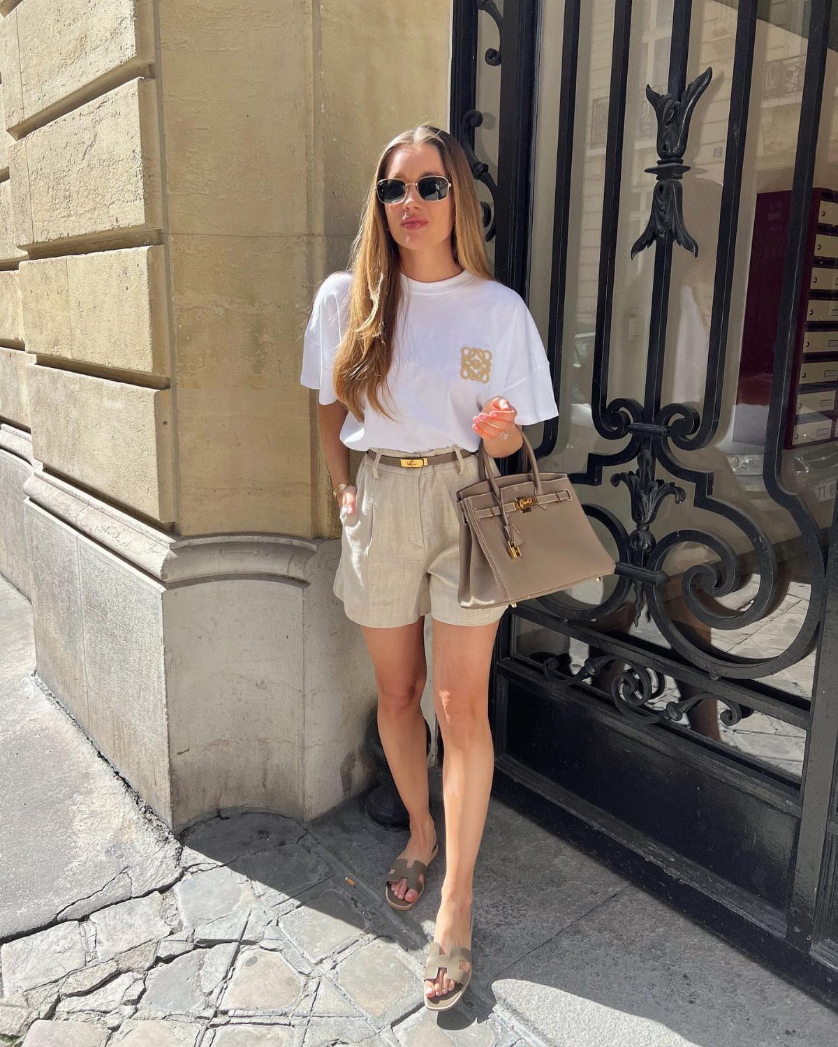 Woman wearing a white t-shirt and cream tailored shorts with a beige handbag.