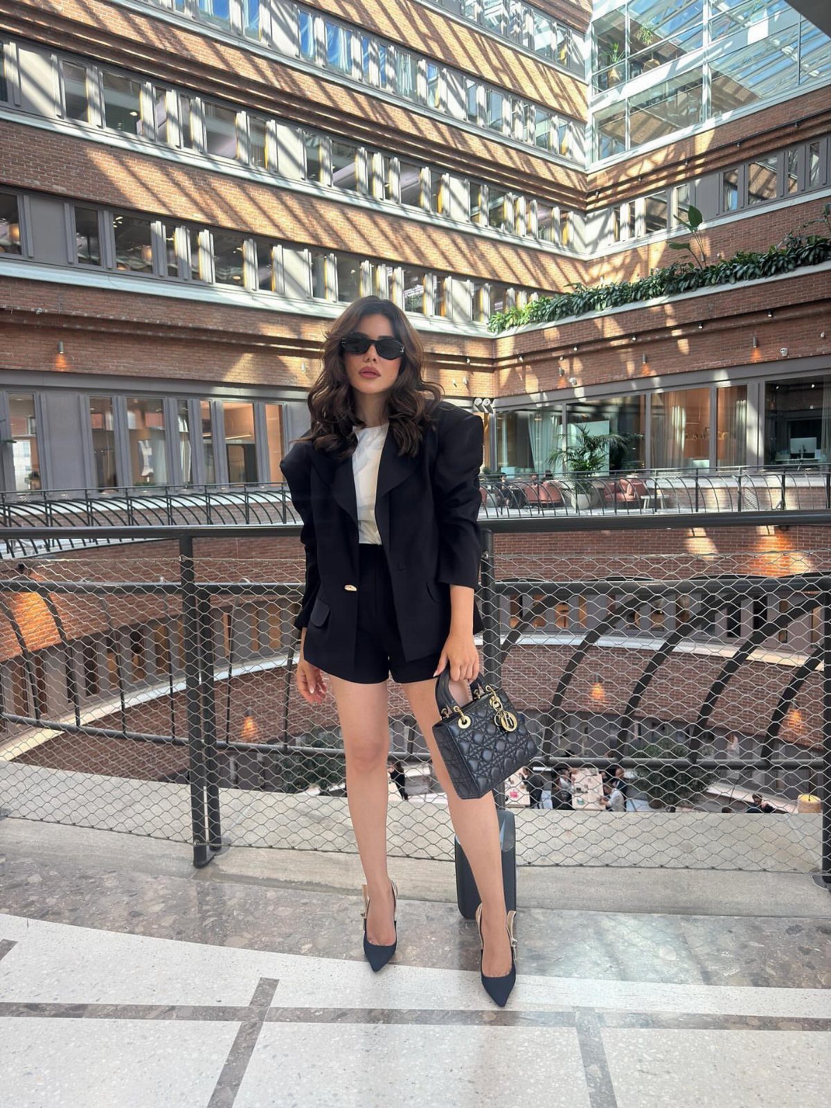 Woman in black blazer and shorts with pointed-toe pumps standing on a balcony.