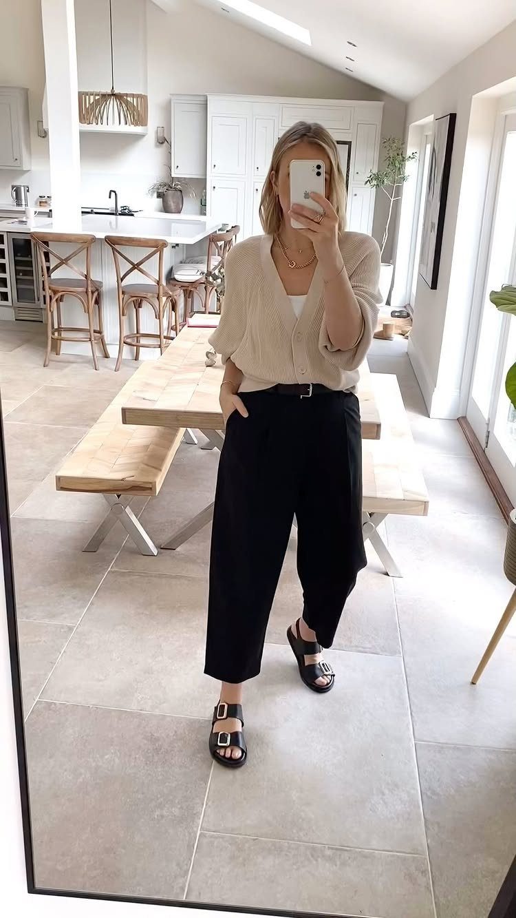 Woman wearing a beige cardigan and black tapered trousers with black sandals.