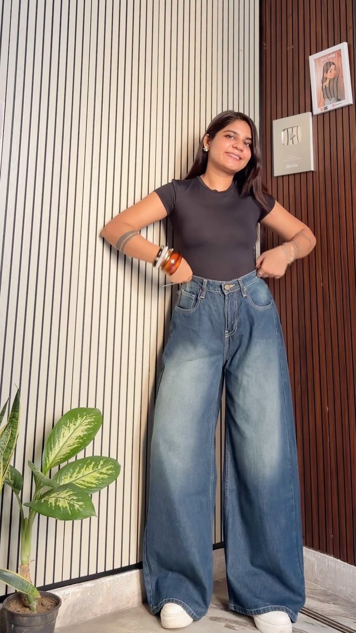 Woman wearing a black top and high-waisted wide-leg blue jeans standing indoors.