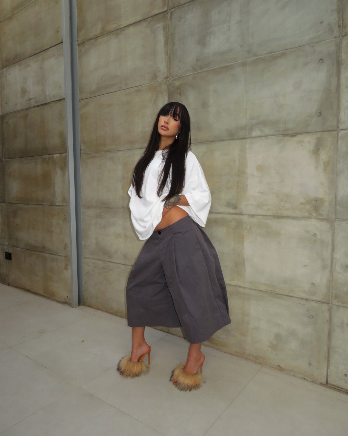 Woman wearing a white cropped top and wide-leg grey cropped trousers against concrete wall