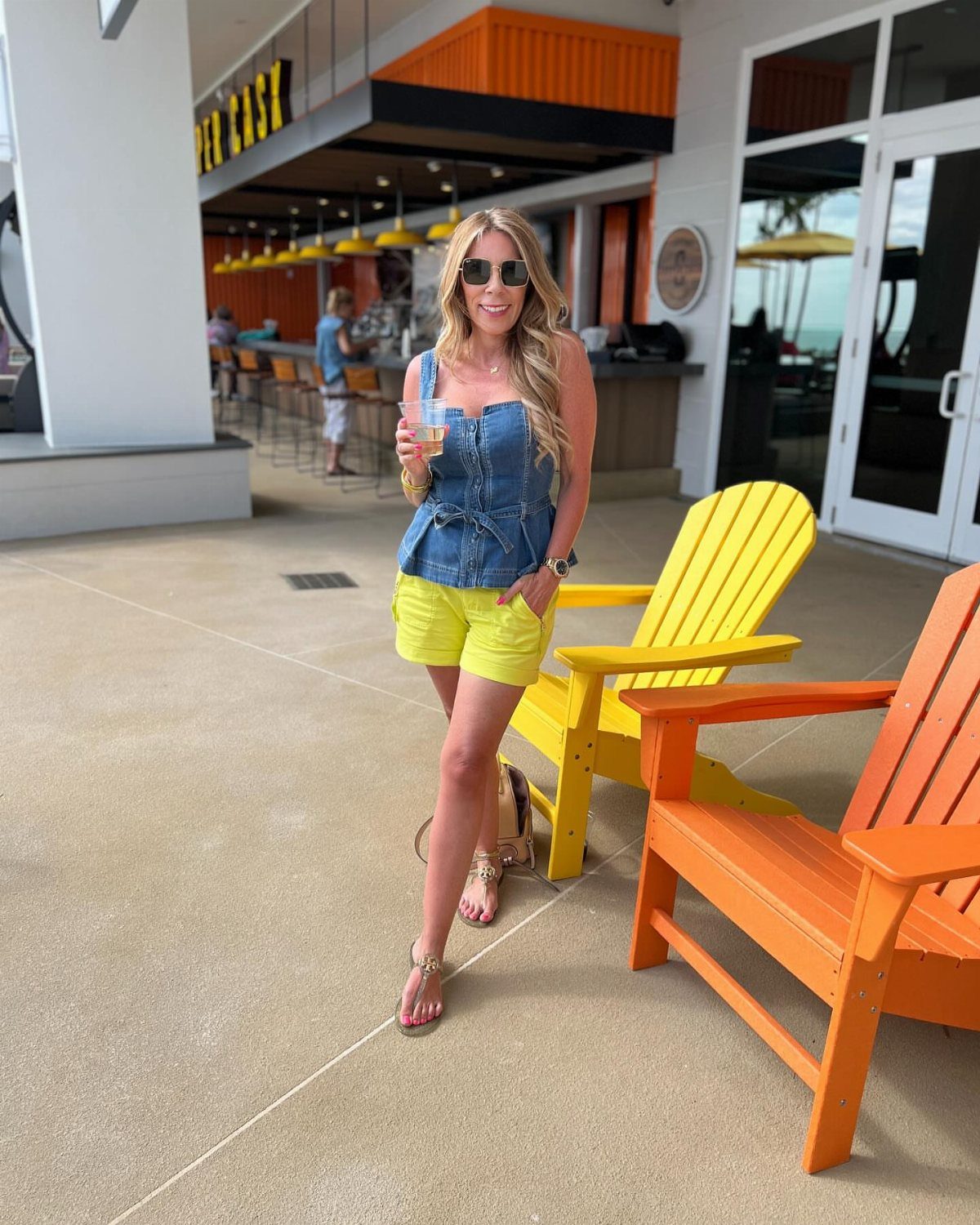 Woman in denim top and yellow shorts standing by colorful beach chairs.