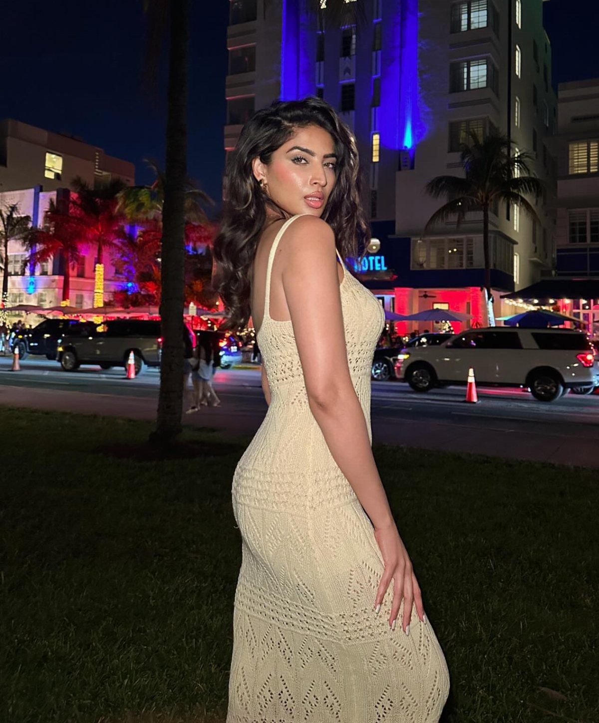 Woman in a beige crocheted maxi dress posing in a city at night.