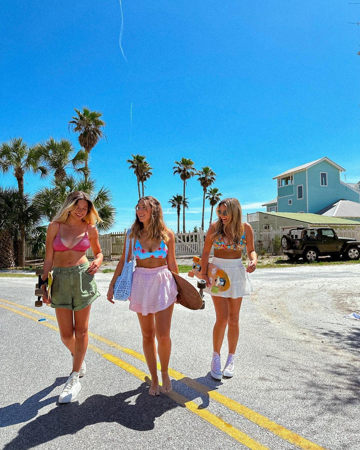 Three women wearing bikini tops and high-waisted shorts walking on a sunny street.