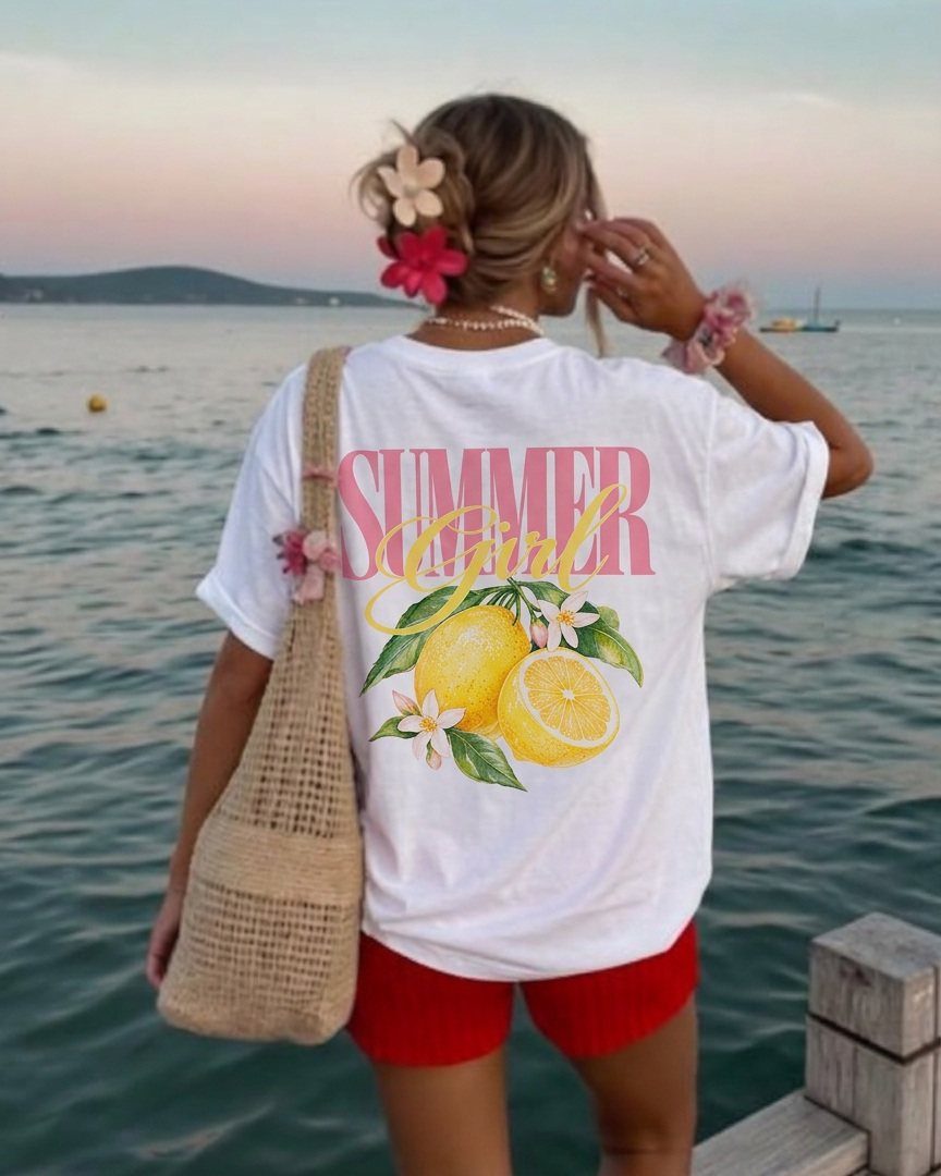 Woman wearing oversized white lemon graphic tee and red shorts by the ocean.
