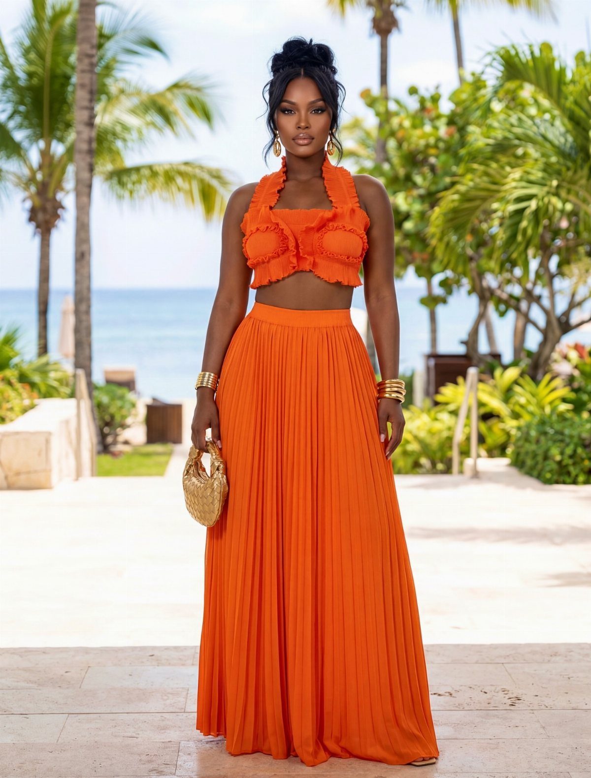 Woman in orange ruffled crop top and pleated maxi skirt by the ocean