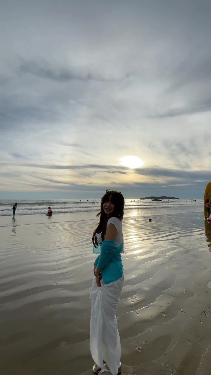 Woman in a long white dress and blue shawl posing on a beach at sunset