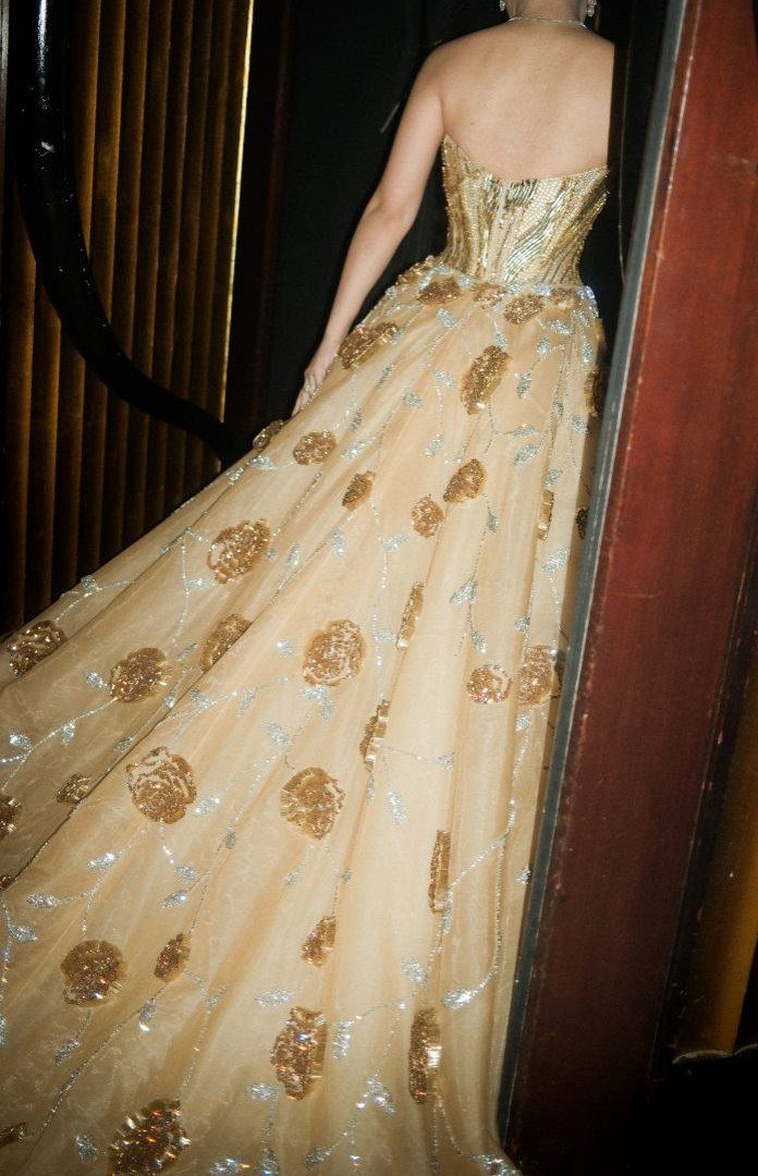 Woman wearing a strapless gold gown with large sequined floral patterns on the skirt.