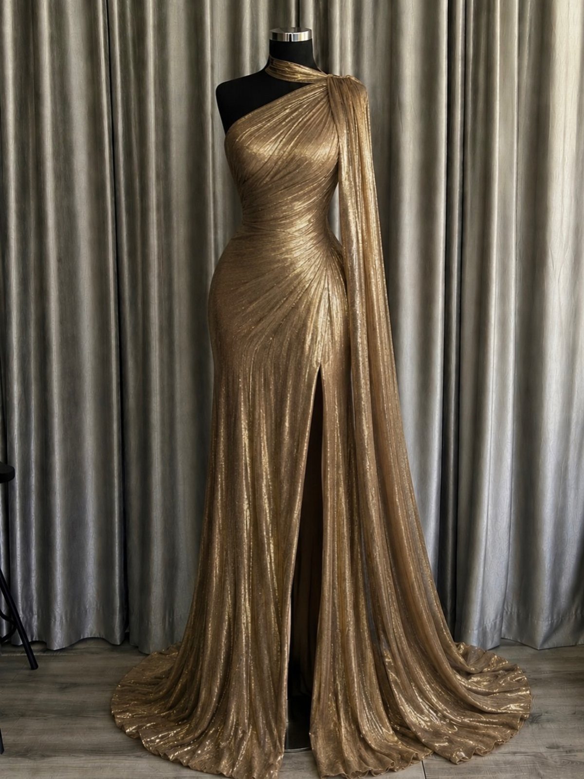 Gold one-shoulder floor-length gown with metallic pleats displayed on a mannequin.