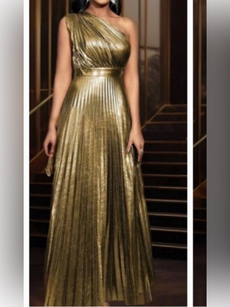 A woman posing in a shimmering, one-shoulder gold pleated metallic maxi dress.