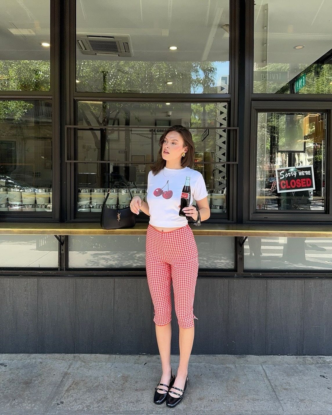 Woman wearing a white cherry t-shirt and red gingham capri pants standing outdoors.