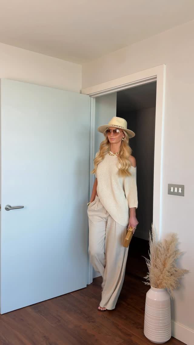 Woman wearing a cream off-the-shoulder top and wide-leg trousers with a straw hat.
