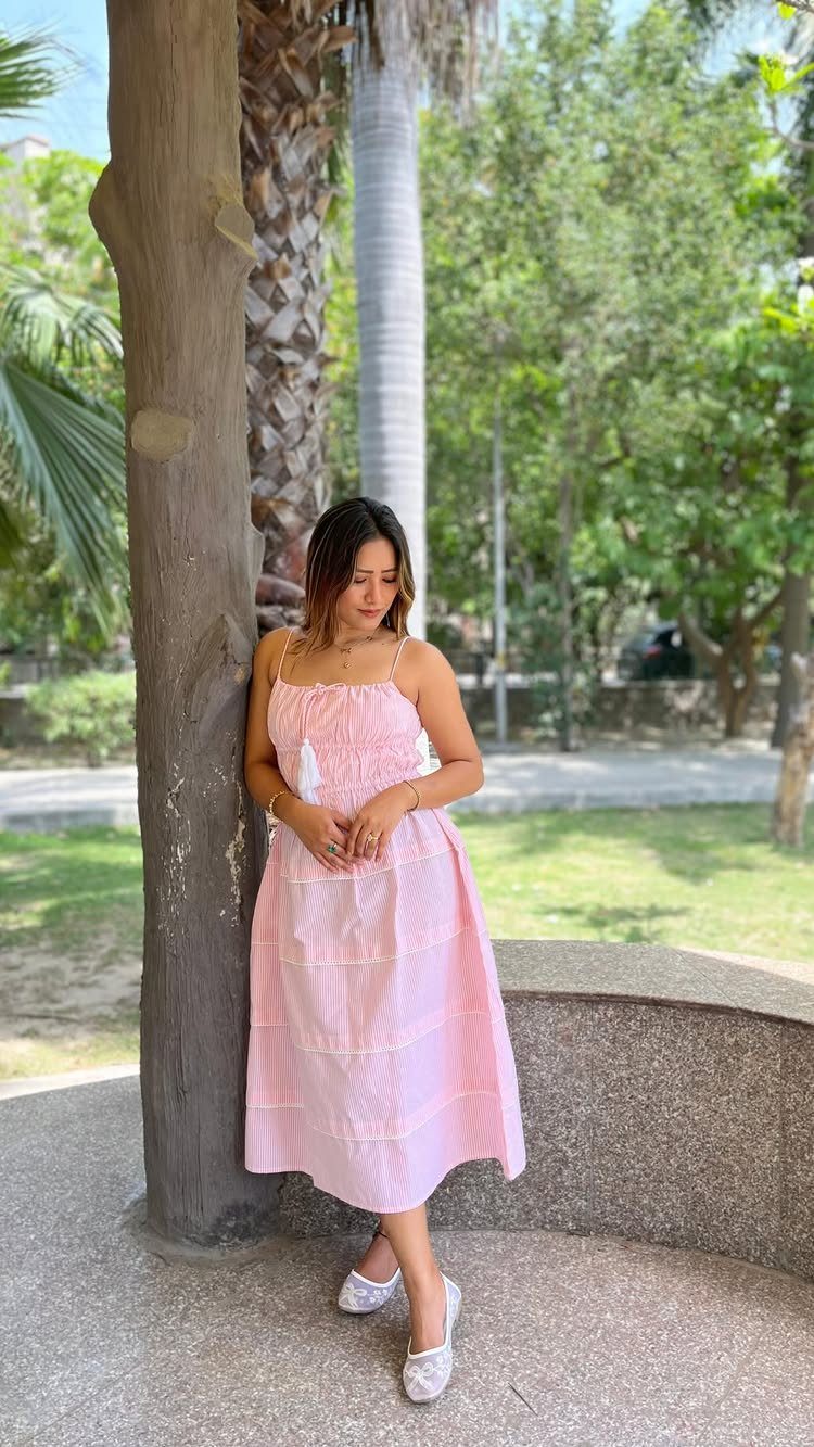 Woman wearing a pink and white striped summer dress leaning against a tree.