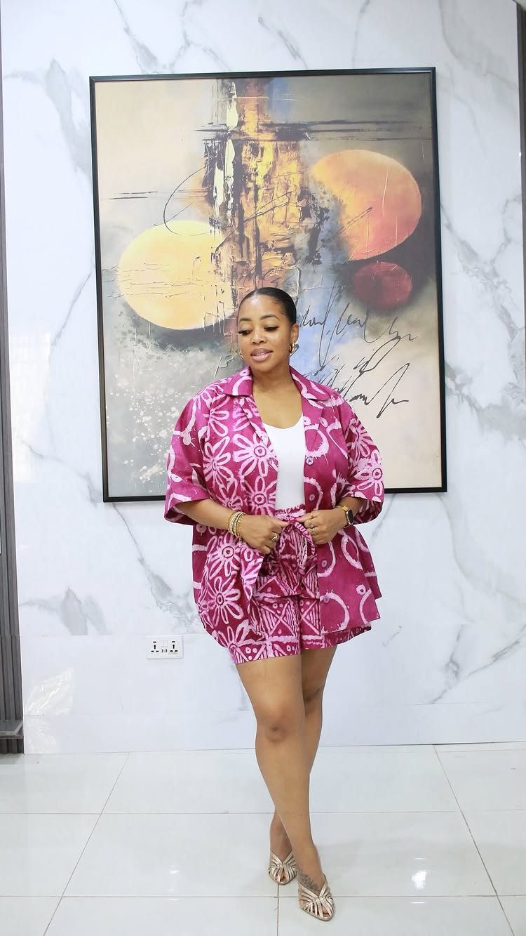 Woman wearing a pink floral print matching shirt and shorts set with white top.