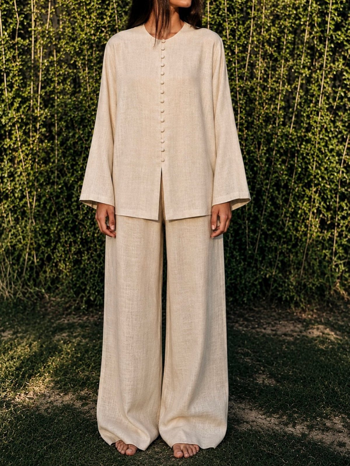 Linen Fashion Women: 6 Outfit Upgrades for 2026 4 Woman wearing a cream linen two-piece set with wide-leg pants standing before a green hedge.