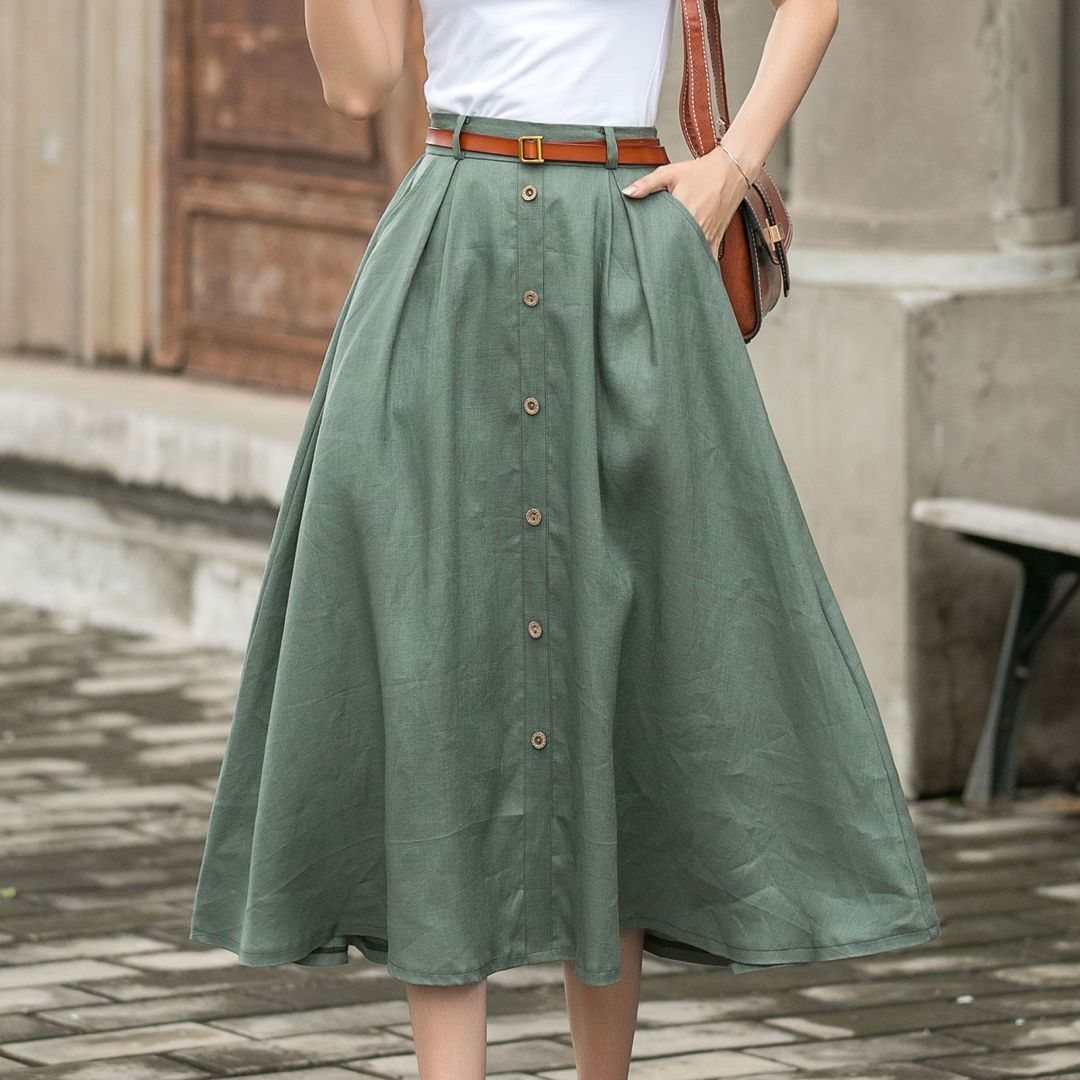 Linen Fashion Women: 6 Outfit Upgrades for 2026 3 A woman wearing a long, sage green button-front linen skirt and a white top.