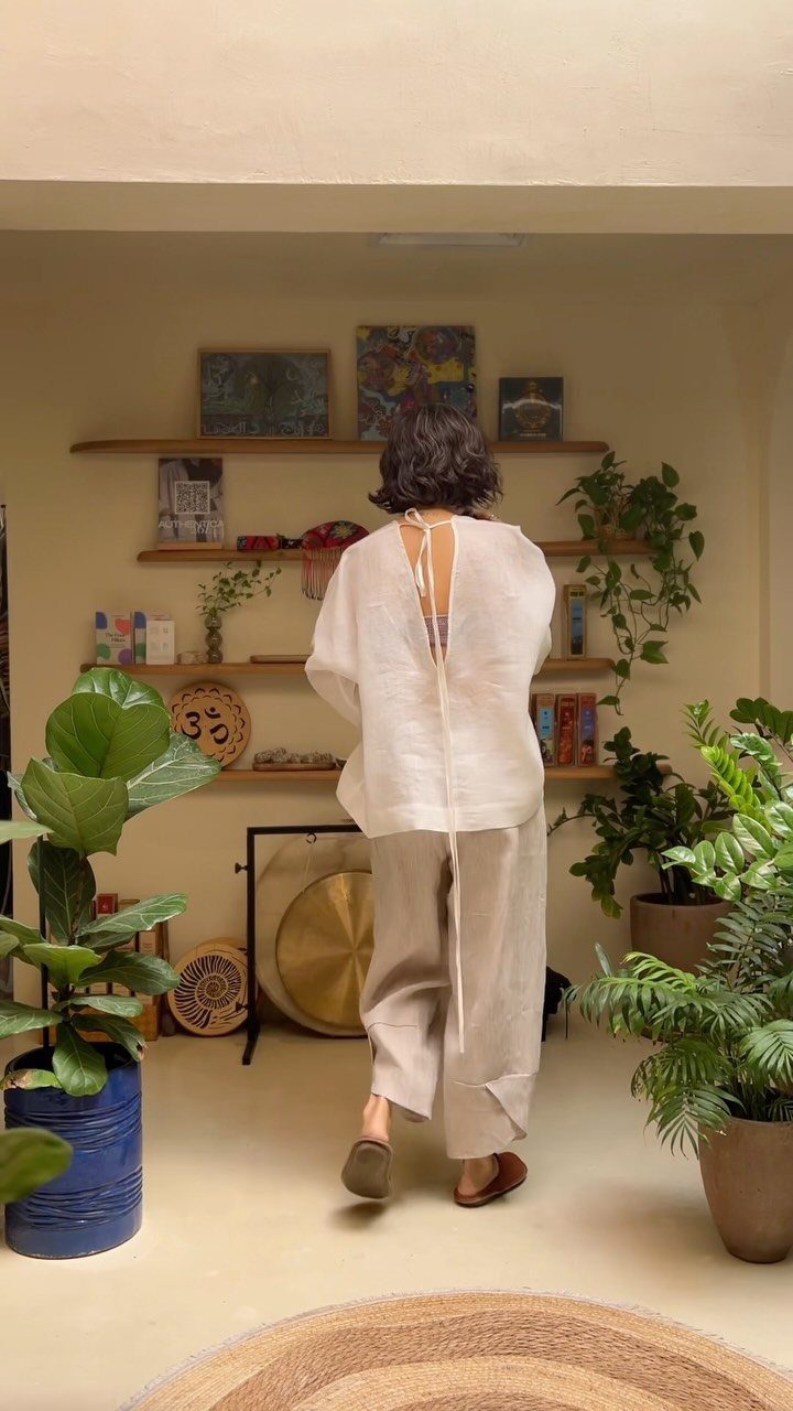 Linen Fashion Women: 6 Outfit Upgrades for 2026 5 Woman walking in a room wearing a white linen blouse and beige linen pants.