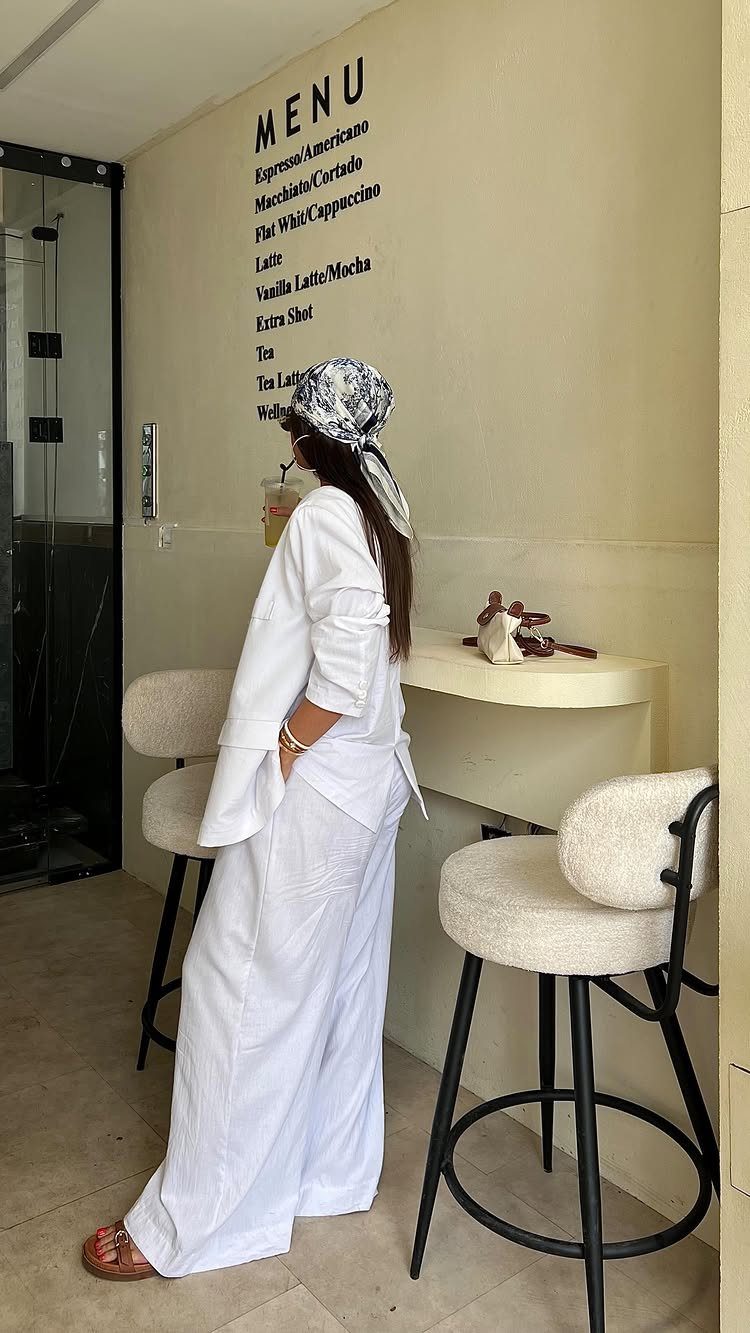 Woman in white linen pants and a white blazer standing by a cafe menu.