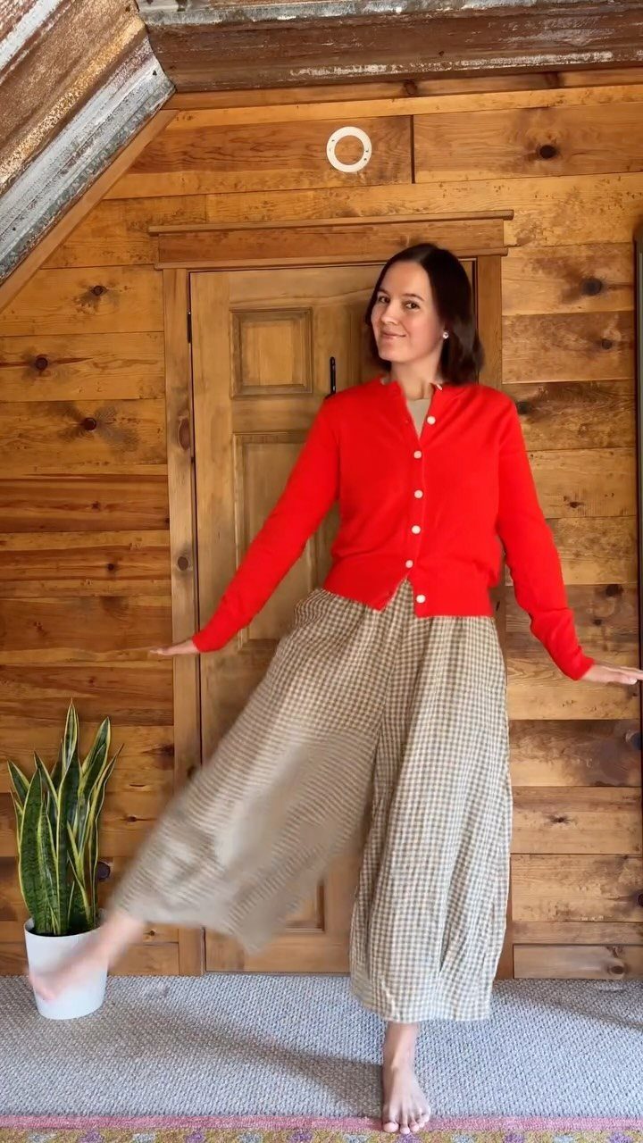 Woman posing in a red cardigan and wide-leg patterned linen pants against a wooden wall.