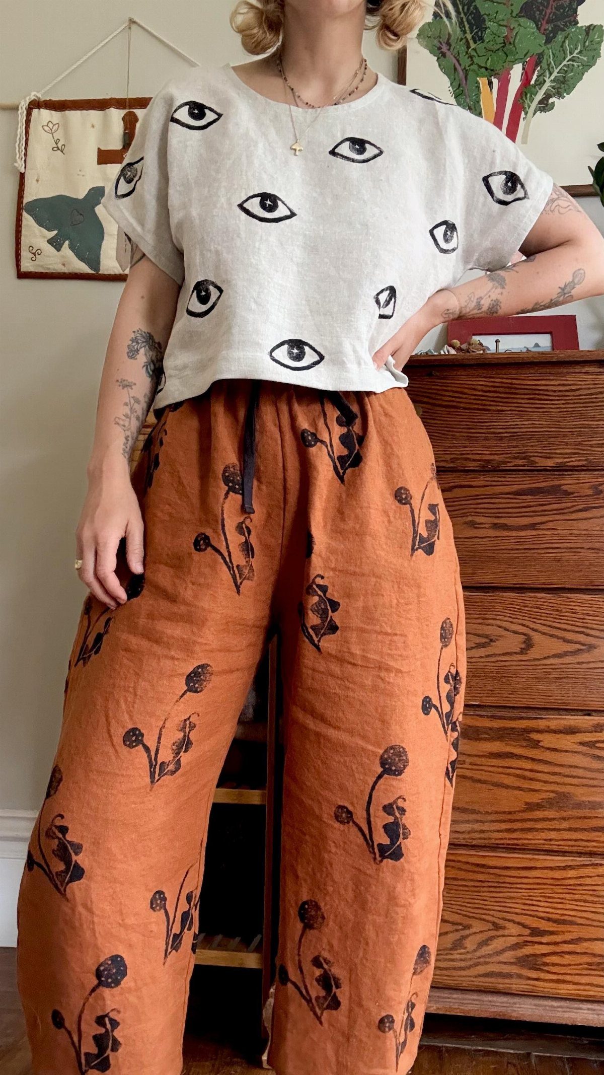 Person wearing a white eye-patterned t-shirt and orange floral linen pants.