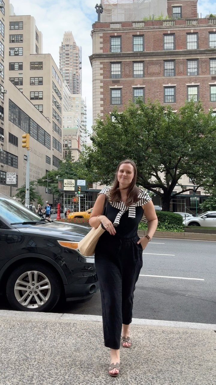 Woman in black linen pants and a striped tank top standing on a city street.