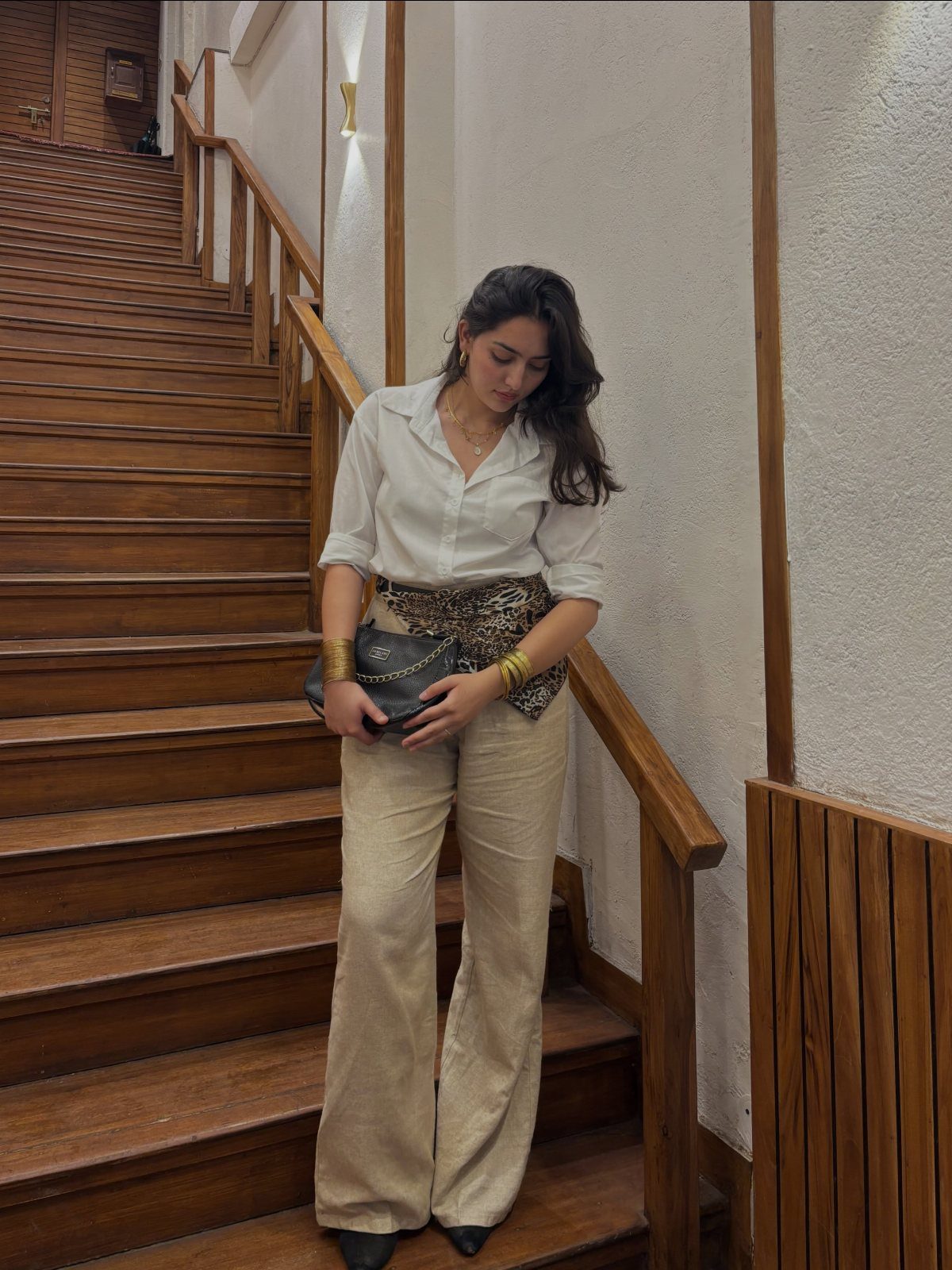 Woman in beige linen pants and white shirt posing on wooden stairs.
