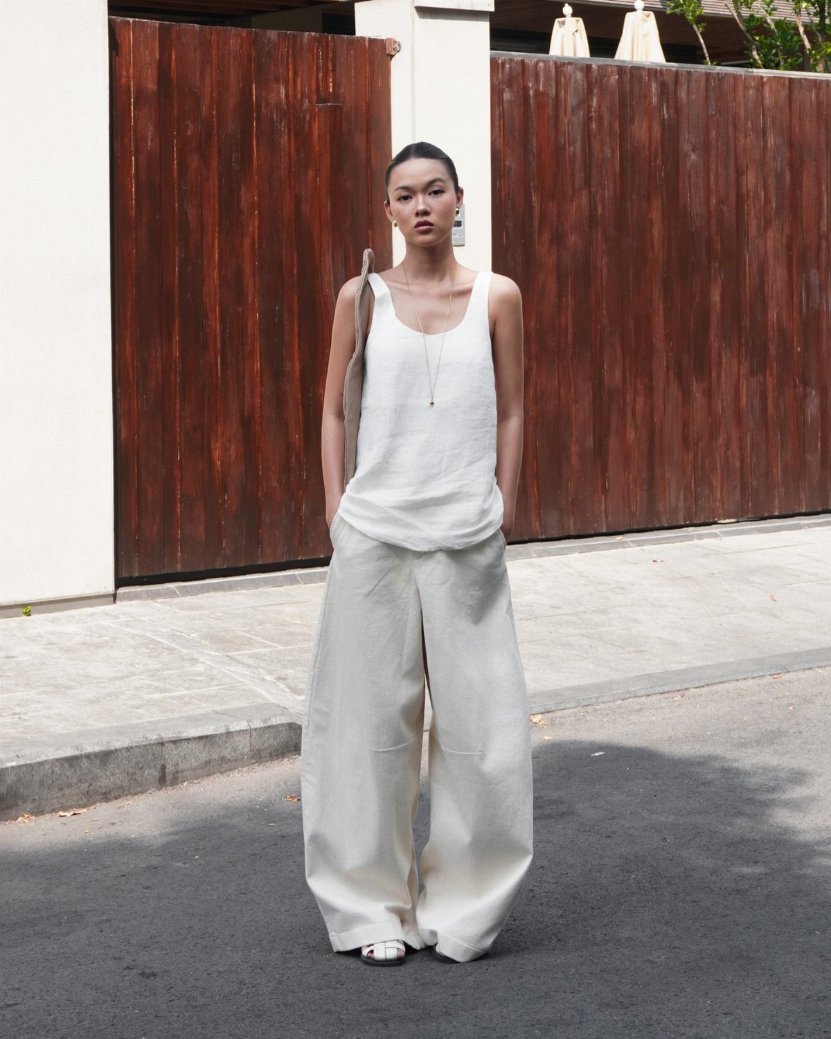 A person wearing a white linen tank top and wide-leg cream trousers standing outdoors.