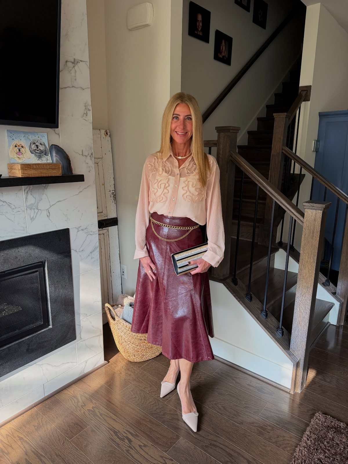 Woman wearing a sheer pink blouse and burgundy leather maxi skirt with gold belt.