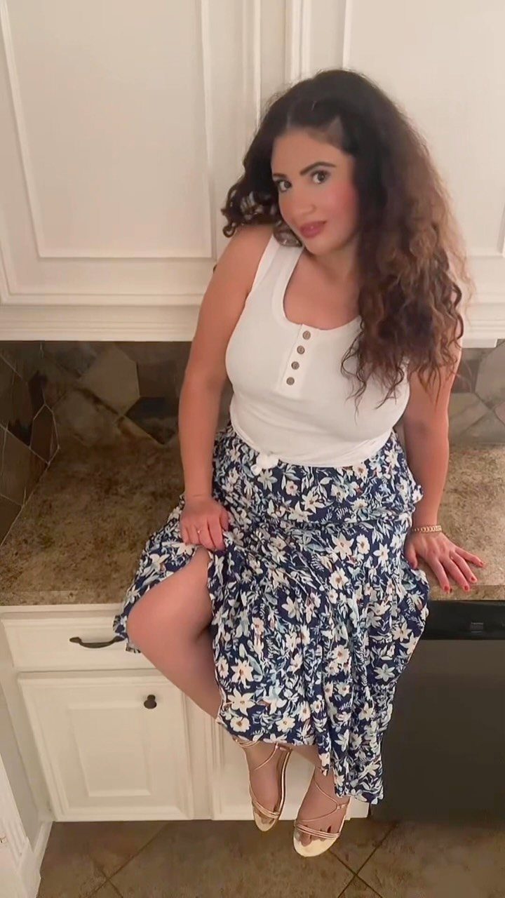 Woman wearing a white top and blue floral maxi skirt with gold heels.