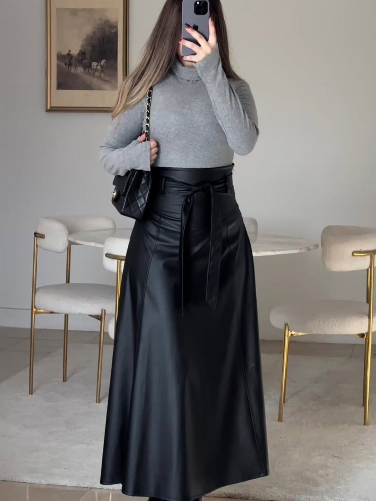 Person wearing a grey turtleneck and a black leather maxi skirt with a tie belt.