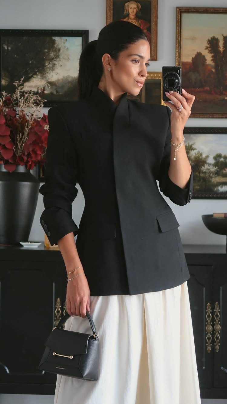 Woman in a black structured blazer and white slim maxi skirt taking a selfie.