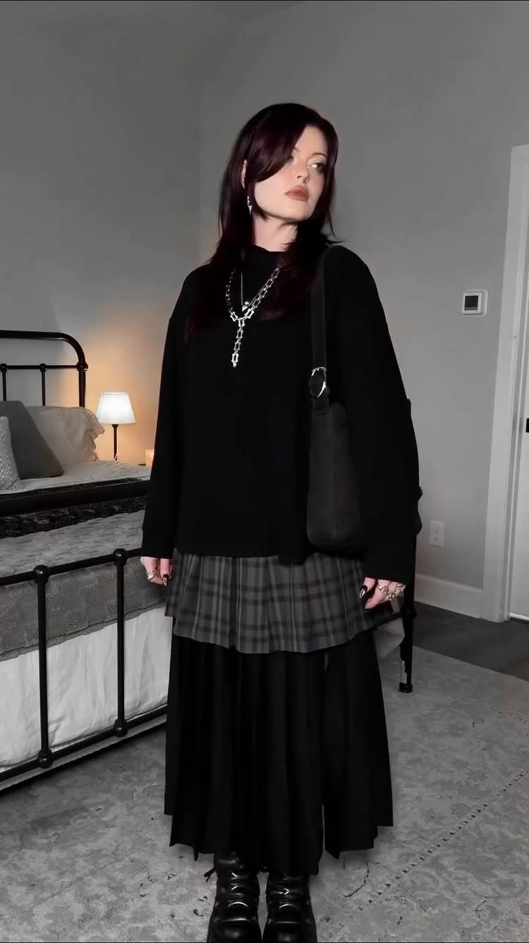 Person wearing a grey plaid skirt over a black maxi skirt and chunky boots.
