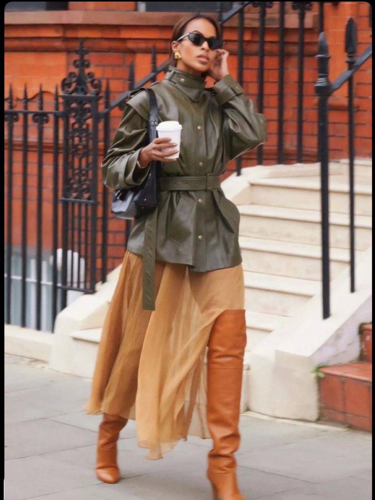 Woman in olive leather jacket and sheer tan maxi skirt with brown boots.