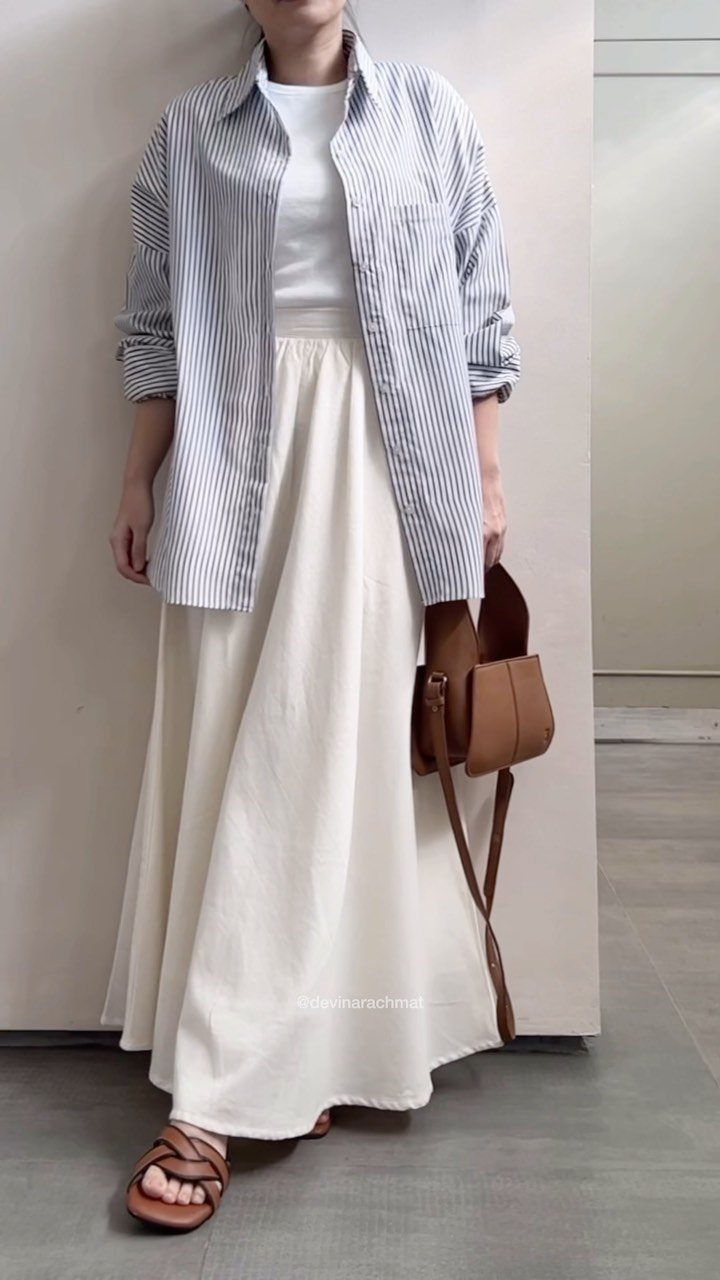 Person wearing a blue striped shirt and white maxi skirt with brown sandals.