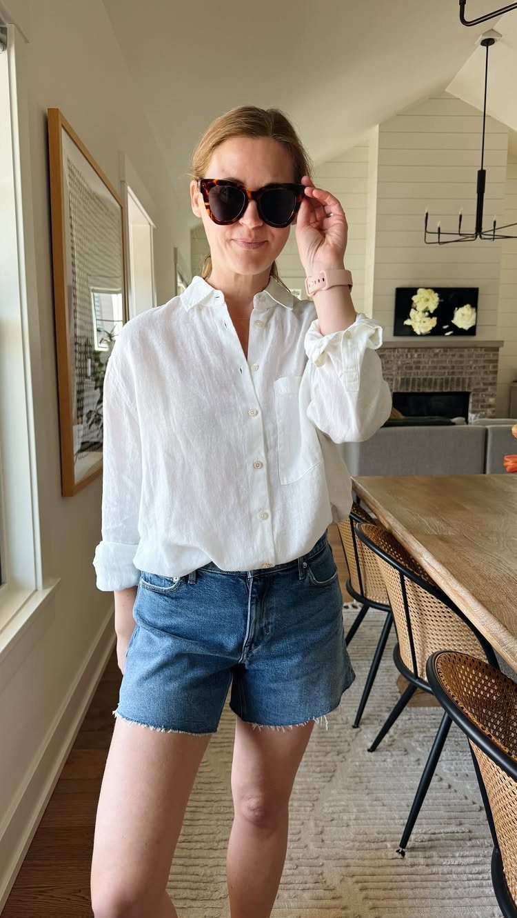 Woman wearing a white linen shirt and blue denim shorts with dark sunglasses.