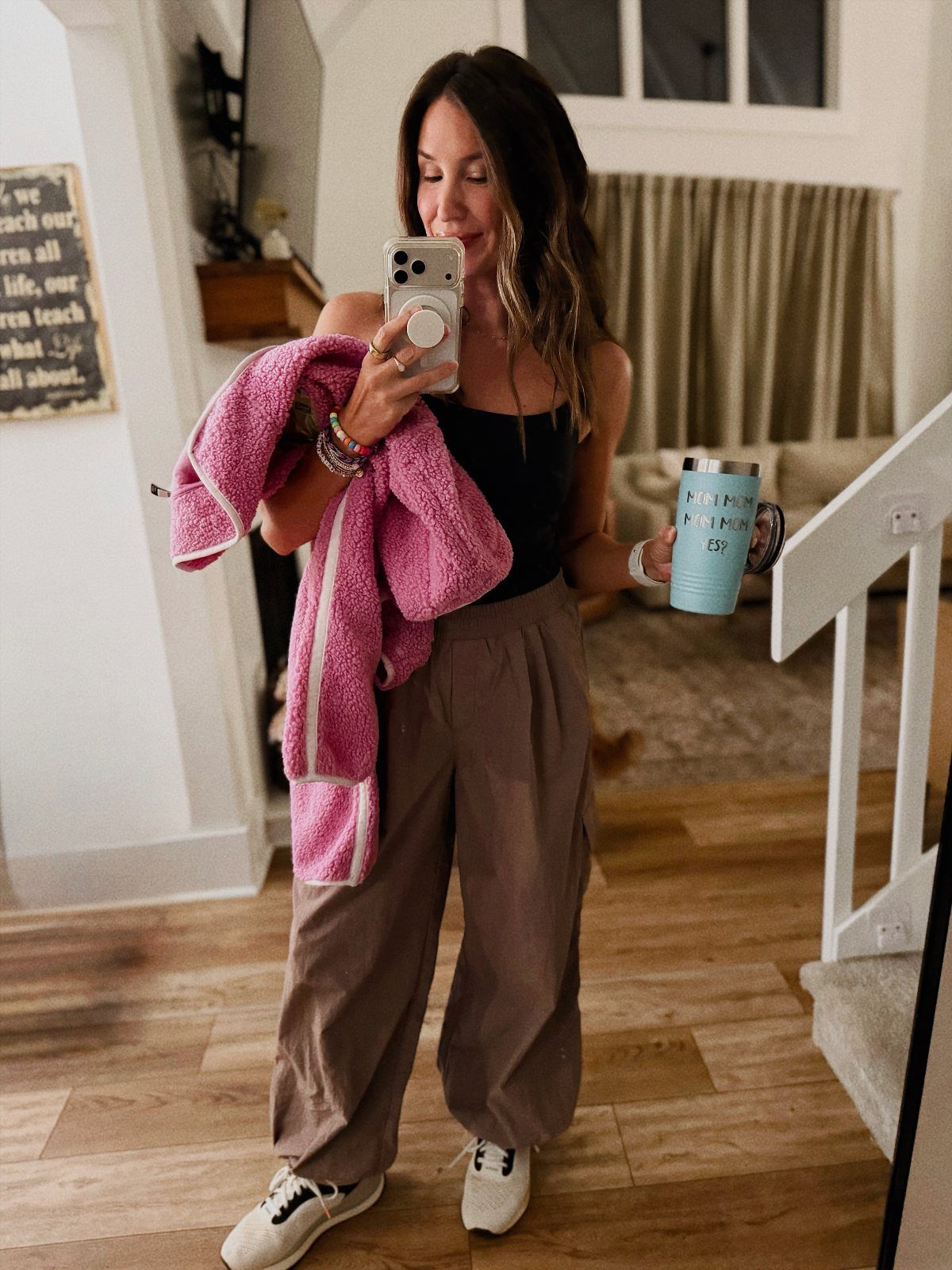 Woman wearing brown parachute pants, black tank top, and white sneakers in a home.