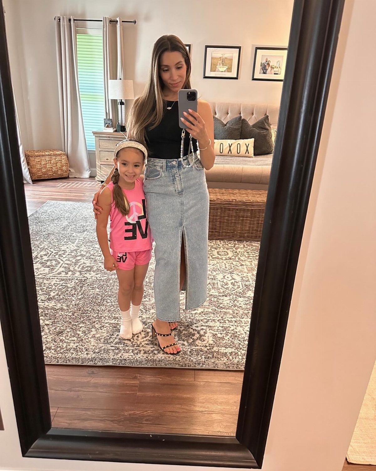 Woman in black tank and long denim skirt posing with daughter in pink outfit.