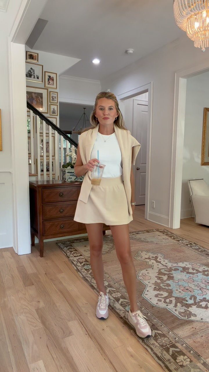 Woman wearing a beige skort and matching jacket with white sneakers and t-shirt.