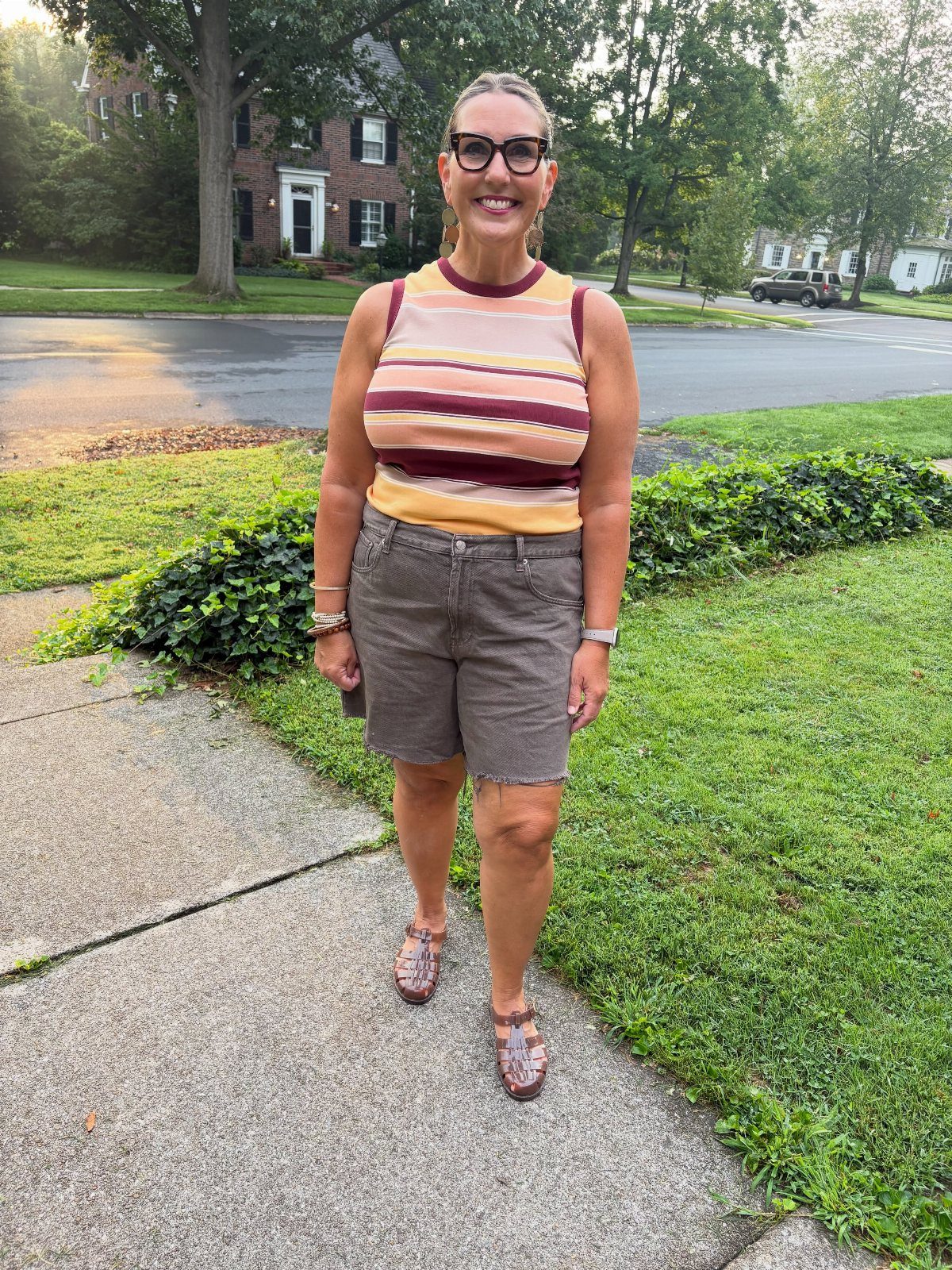 Woman wearing a striped sleeveless top, brown denim shorts, and patterned sandals outdoors.