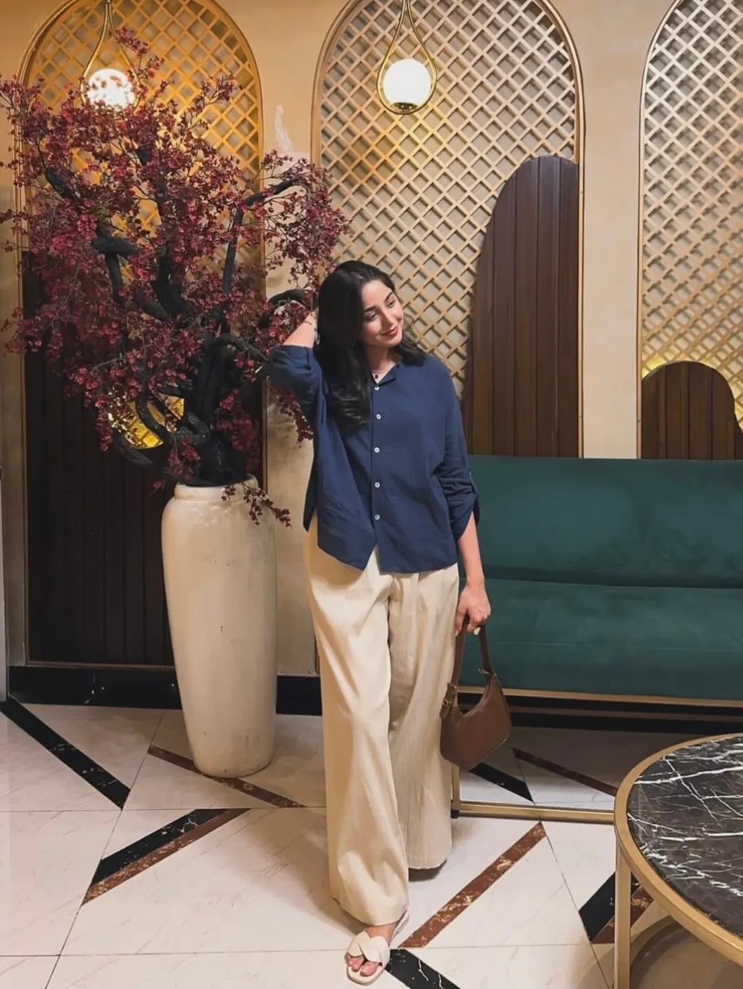 9 Navy Blue Outfit Ideas for Every Setting 3 Woman wearing a navy blue button-down shirt and cream wide-leg trousers standing in a decorated room.